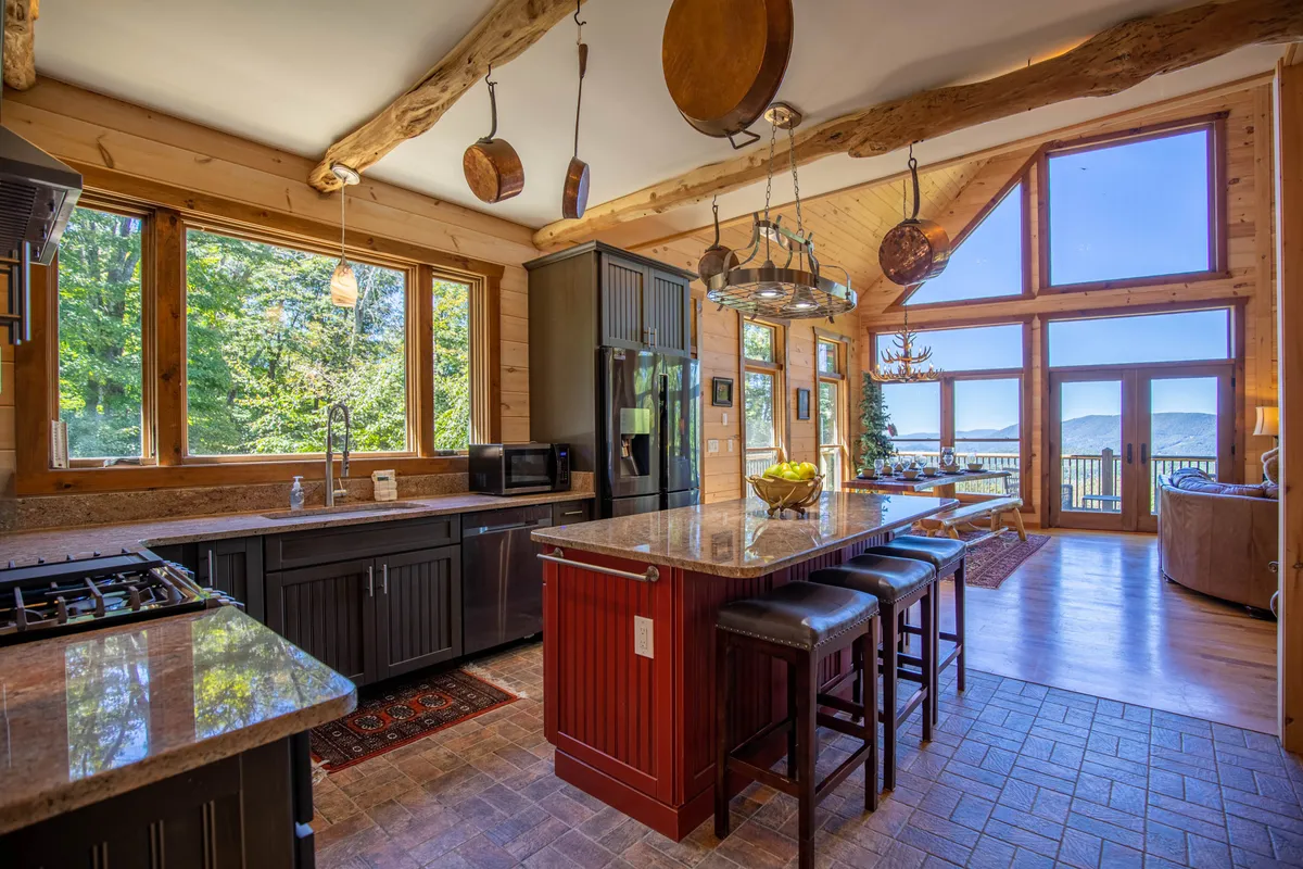 An elegant kitchen and dining area, featuring an island countertop, large windows, rustic wood beams, and stainless steel appliances. The layout flows naturally into a dining space filled with light and mountain views, echoing the home's open design.