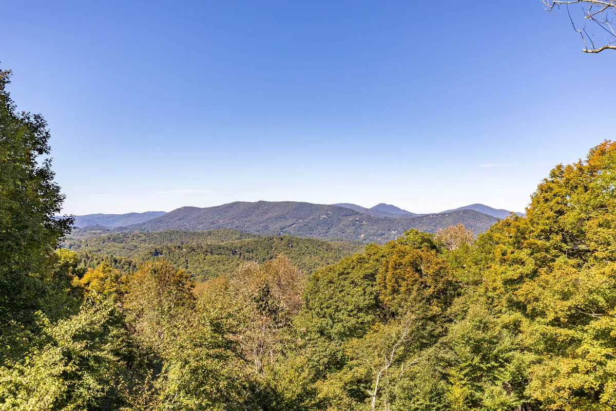 An expansive view image showcasing a beautiful mountain range under a clear blue sky, with dense foliage in the foreground. The photo evokes the high-altitude setting and the stunning natural landscape that surrounds the property, inspiring thoughts of hiking and outdoor exploration.