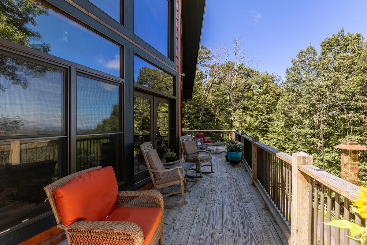 The exterior deck features comfortable seating and is surrounded by lush greenery, with a scenic mountain view in the background. The inviting setup suggests relaxation, socializing, and enjoying the natural environment without sacrificing comfort.