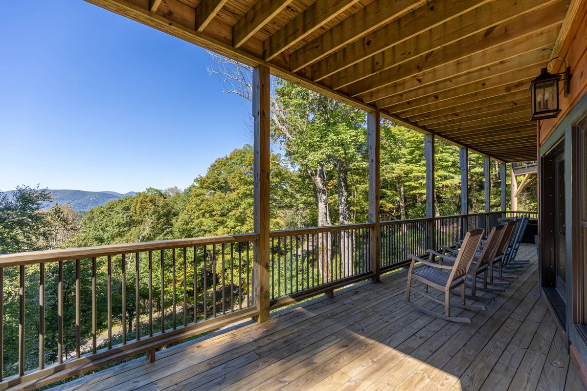 This image shows a tranquil wooden deck featuring classic rocking chairs and a sturdy railing, set against a backdrop of sweeping mountain vistas. The view is open and inviting, suggesting a perfect spot for both people and pets to unwind while enjoying the fresh mountain air.